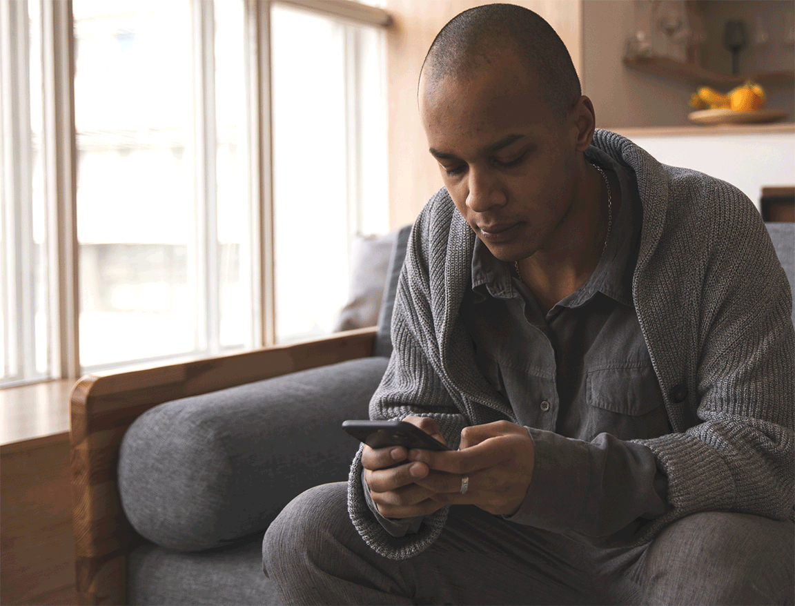 A man sitting by a bright window while looking at his phone
