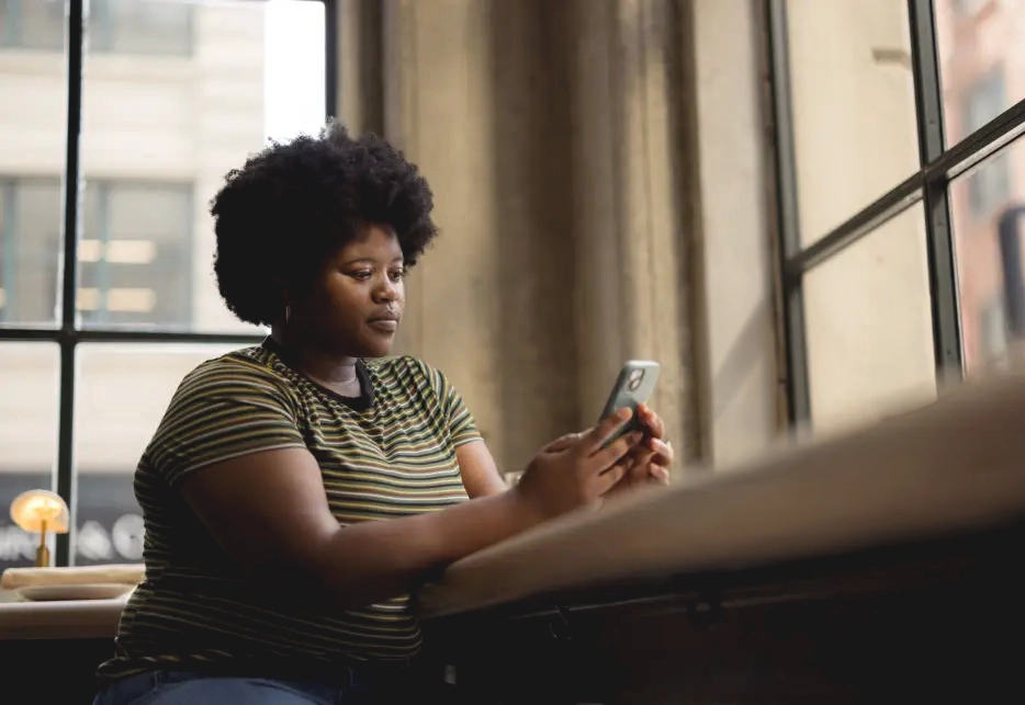 A person sitting near a window and using a phone