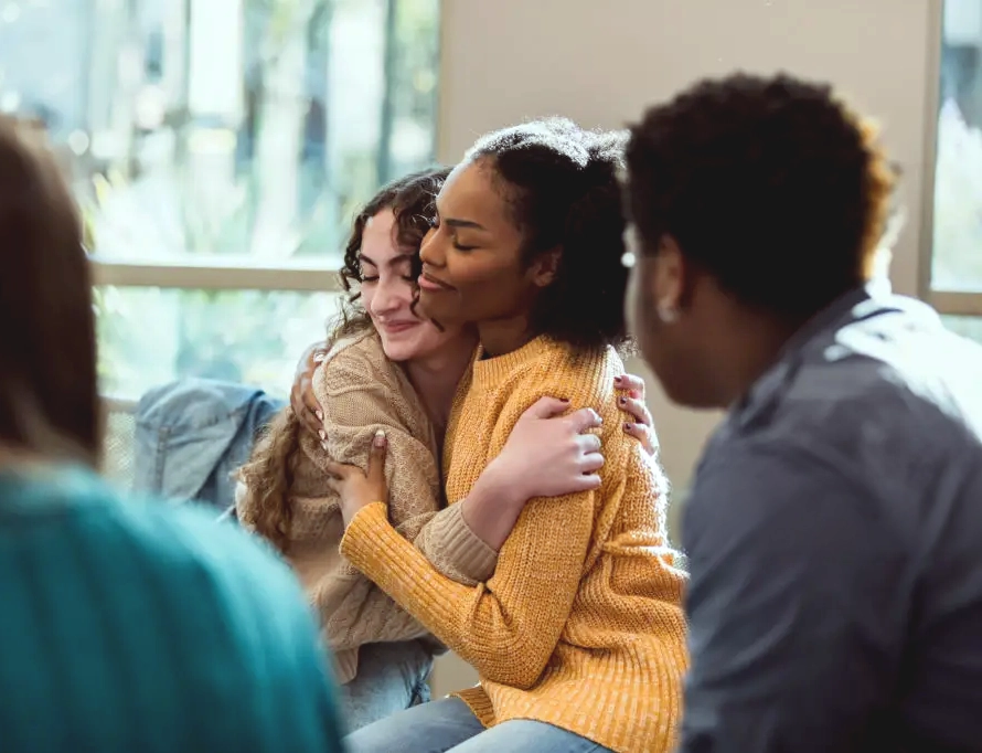 Two people embracing during a supportive group conversation