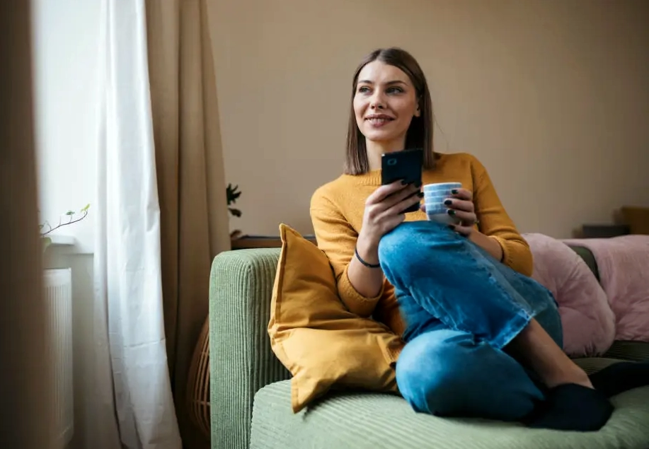 A person sitting calmly with a phone and mug near a window